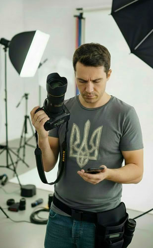 Фотограф у студії з камерою Nikon і смартфоном у руках